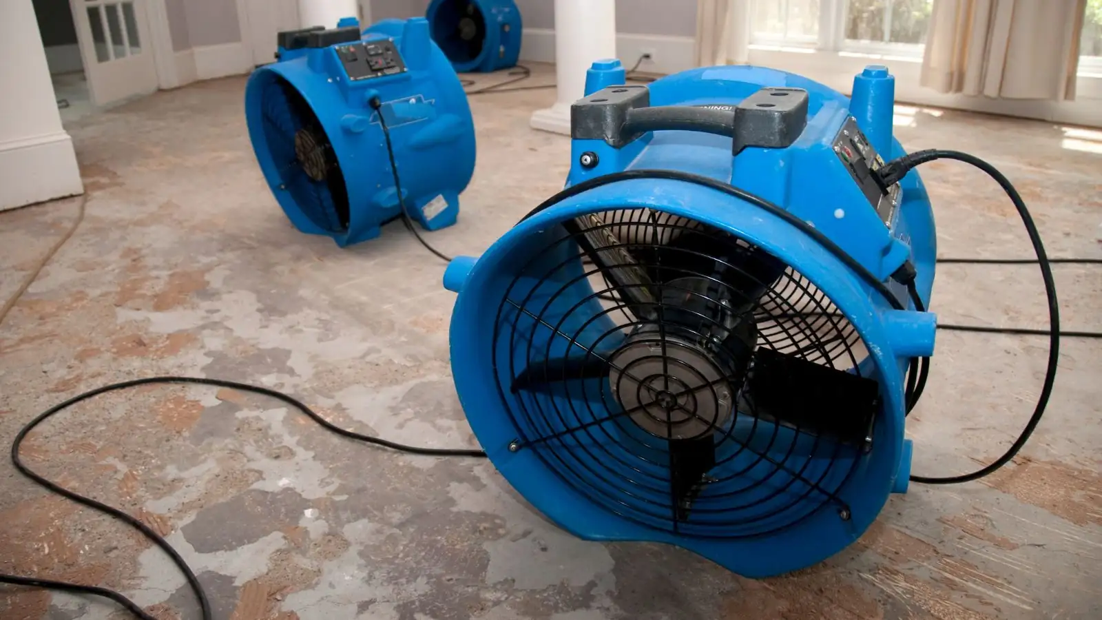 Blue air movers running on a damp floor during structural drying