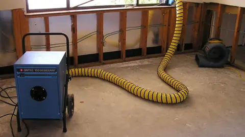 Desiccant dehumidifier with a yellow duct in a room where the lower wall has been opened
