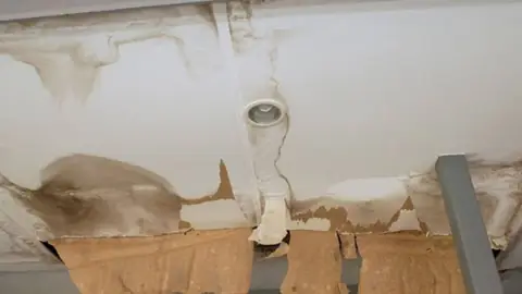 Water-damaged ceiling with peeling drywall paper around a pipe