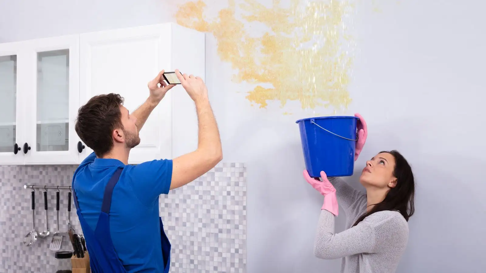 Man photographing a stained wall while a woman holds a bucket underneath