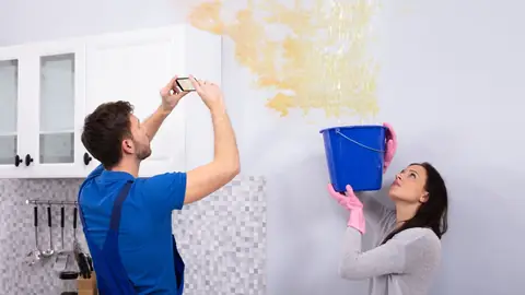 Man photographing a stained wall while a woman holds a bucket underneath
