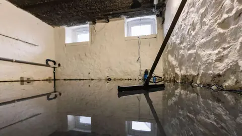 Squeegee pushing water across a flooded basement floor beside a stone foundation wall