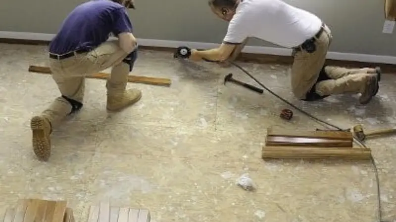 Two workers kneeling on a subfloor while preparing for new flooring